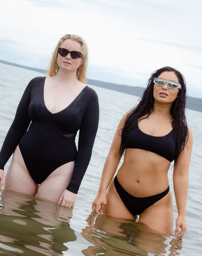 SWMR The Dip low rise bikini bottom in black worn at the beach with another model in a black paddle suit